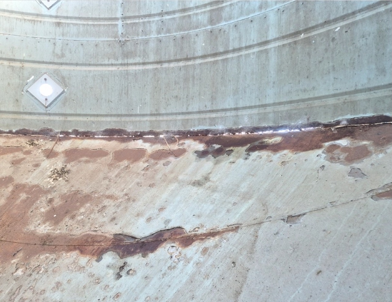 Silo interior before blasting — band of heavy rust and failed coating across the steel wall